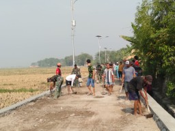 TNI dan warga gotong royong meratakan tanah untuk pemasangan paving
